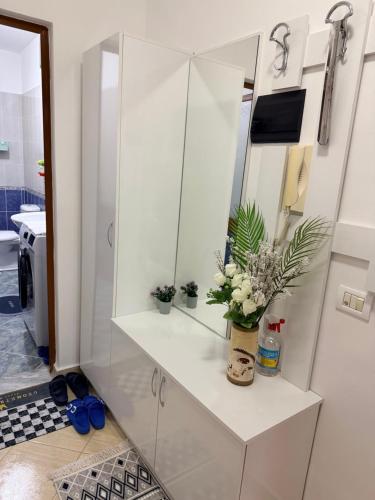 a white bathroom with a mirror and flowers on a counter at ASA Apartament in Tirana