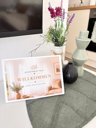 a sign on a table with flowers and a tv at Apartment Niki in Siegendorf im Burgenland