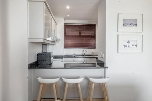 a kitchen with three bar stools and a counter at Azure Guesthouse in Ballito