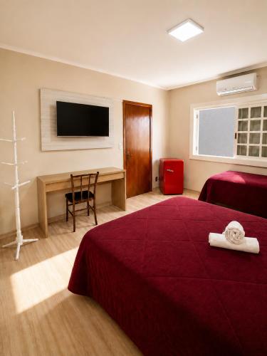 a hotel room with a bed and a desk and a television at Guest house - Casa do Rogério in Caxias do Sul