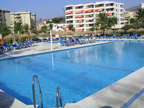 a large swimming pool with blue chairs and umbrellas at Nogalera Boutique Apartment in Torremolinos