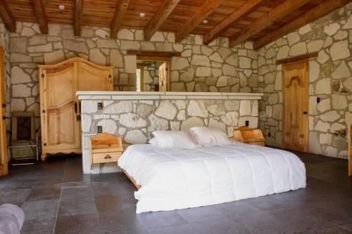a bedroom with a white bed in a stone wall at Finca en el Bosque Huasca de Ocampo con Alberca in Huasca de Ocampo