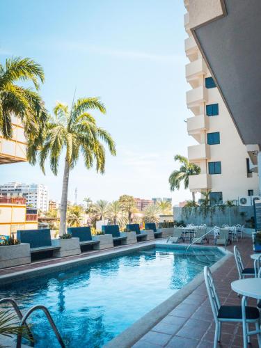 a swimming pool with chairs and palm trees and a building at Hotel Puerto Playa Suites in El Morro de Barcelona