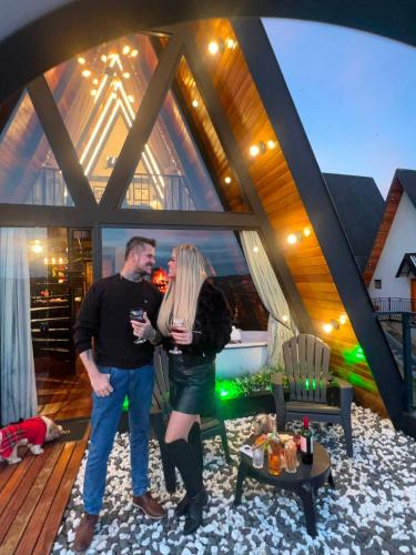 a man and woman standing in a living room with wine glasses at Chalé Super Luxo Monte Lorobell in Campos do Jordão