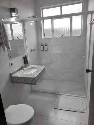 a white bathroom with a sink and a shower at Hotel Palmeiras in Laranjeiras do Sul
