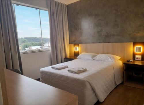 a bedroom with a bed and a large window at Hotel Palmeiras in Laranjeiras do Sul