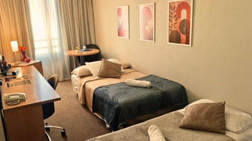 a hotel room with two beds and a desk at Hotel aeroporto Guarulhos in Guarulhos