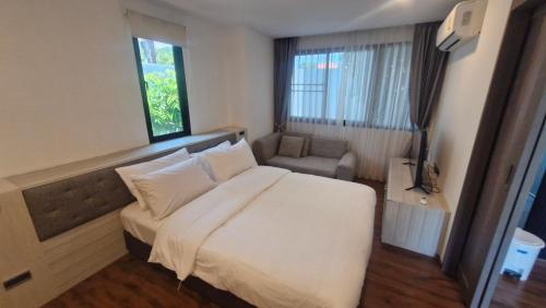 a bedroom with a large white bed and a chair at Stasia Suites Sriracha in Ban Fang Daeng