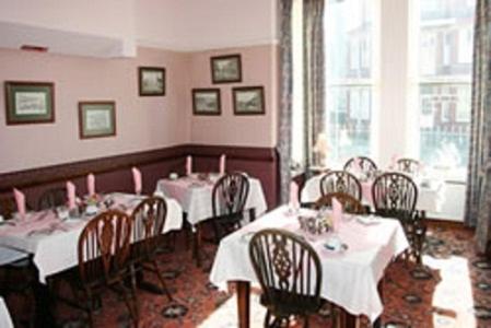 un comedor con mesas y sillas blancas y ventanas en Viking Hotel, en Bridlington