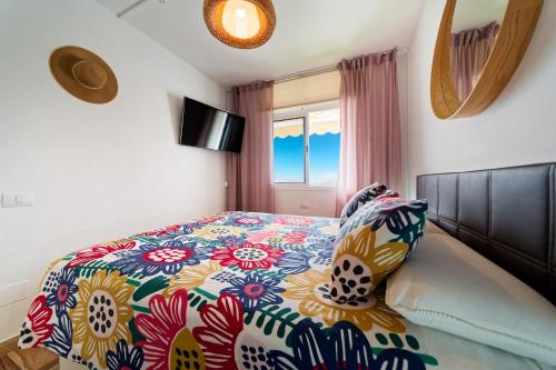 a bedroom with a bed with a colorful comforter and a window at Incredible Sunsets in Puerto Rico de Gran Canaria