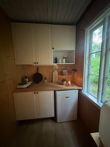 a small kitchen with white cabinets and a window at hytte ved innsjø in Skien