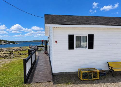 a white house with a wooden walkway and a bench at The Wild Rose Cottage & Bird's Nest in Twillingate