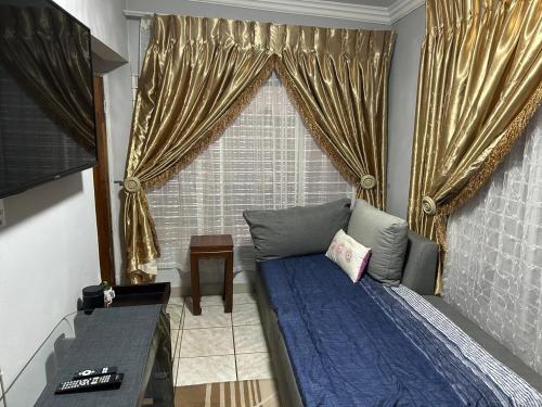 a bedroom with a bed with blue sheets and gold curtains at The Family Room in Krugersdorp