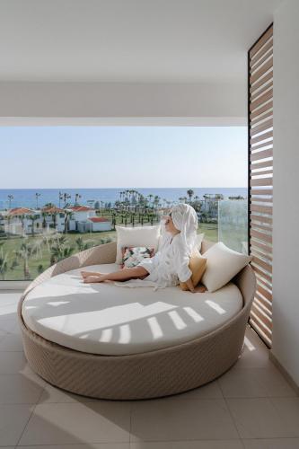 a woman laying on a bed in a room with a window at At Herbal Boutique Hotel & Spa in Protaras