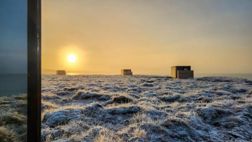a snowy field with the sunset in the background at Mystic Light Lodge in Búðardalur