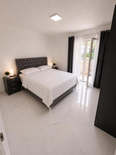 a white bedroom with a bed and a large window at Villa Azar in Dobra Voda