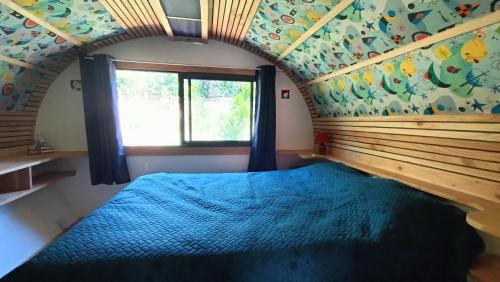 a bedroom with a blue bed in a room with a window at Tiny house chez Manou in Castelnau-de-Mandailles