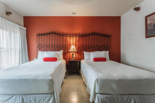 two beds in a hotel room with red walls at Casa Aura Hotel, Mérida in Mérida