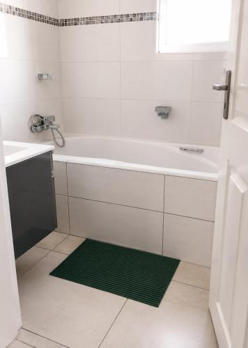 a white bathroom with a tub and a green rug at R&N Hosts in Maseru