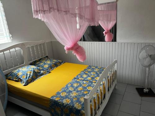 a bedroom with a bed with yellow sheets and pink curtains at Aux bambous in Rivière-Salée