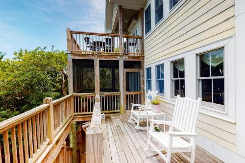 a deck with two white chairs and a balcony at Pink Bird Cottage in Edisto Beach