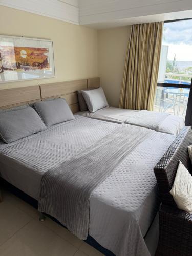 two beds in a hotel room with a window at Hotel tropical Manaus suite luxo in Manaus