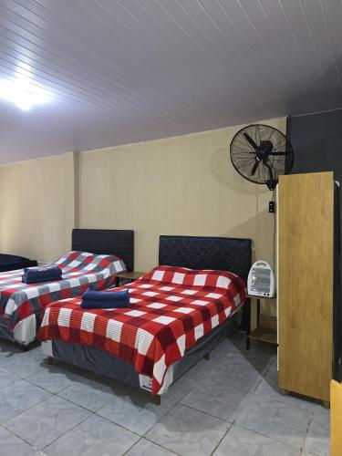 two beds in a room with a fan on the wall at Hummingbird Hostel in Ciudad del Este