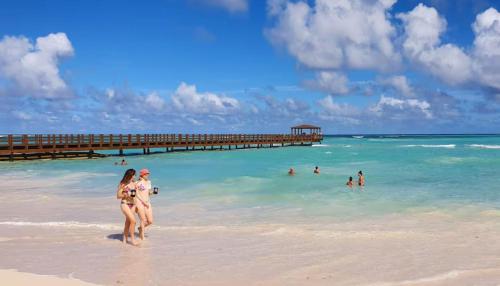 a group of people walking on a beach with a pier at CARIBBEAN DREAMS at SOL CARIBE - LOS CORALES beach in Punta Cana