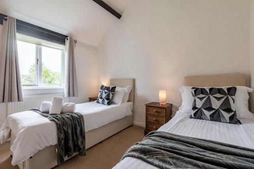 a bedroom with two beds and a window at Braddon - Treworgie Barton Cottages in Bude