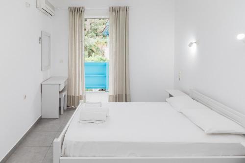 a white bedroom with two beds and a window at Afroditi Pansion in Agios Nikitas