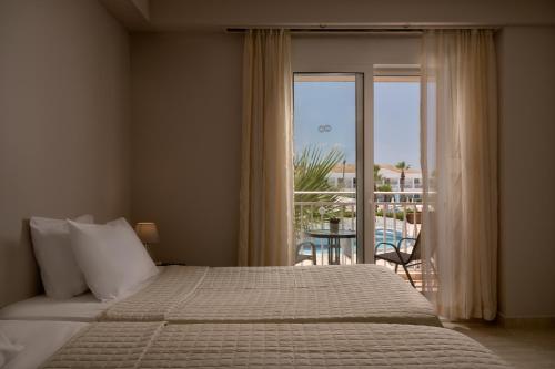 a bedroom with a bed and a view of a balcony at Sandy Beach Resort by Rizos Resorts in Agios Georgios