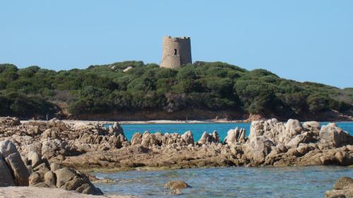 a lighthouse on an island with rocks in the water at Hotel Petri Marini in Aglientu