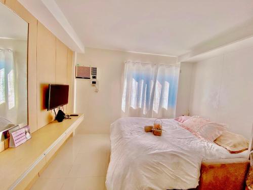 a white bedroom with a bed and a television at Nice location in the persimmon condo in Cebu City