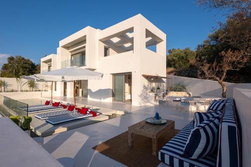 a white house with lounge chairs and an umbrella at CAPO LEFKADA Villa 71 - Sea View - Two Private Pools in Tsoukalades