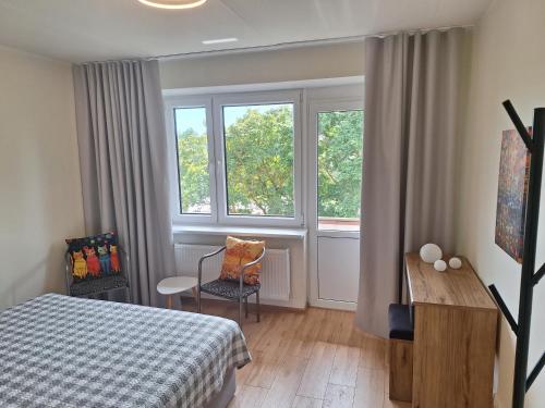 a bedroom with a bed and a desk and two windows at Spacious & sunny apartment with a balcony in Tartu