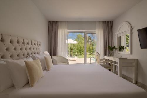 a bedroom with a large white bed and a desk at Sandy Villas Resort by Rizos Resorts in Línia