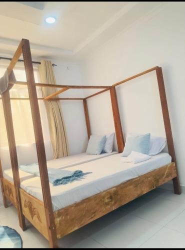 a wooden bed with white sheets and blue pillows at Imani staycation Penthouse Diani in Diani Beach