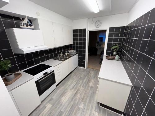 a kitchen with white cabinets and black tiles on the wall at Bakgården Mariestad in Mariestad