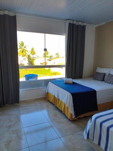 een slaapkamer met twee bedden en een groot raam bij Costa Suítes in Maragogi