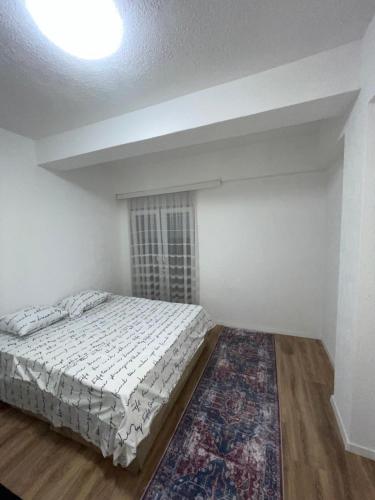 a white bedroom with a bed and a rug at Bleon Apartment in Prizren