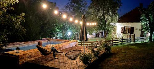 a woman sitting on a deck next to a pool at night at Konak ispod Subjela in Ševrljuge