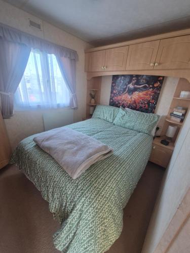 a bedroom with a green bed with a painting on the wall at Mark and Teresa's 8 berth caravan on Coral Beach Ingoldmels in Ingoldmells