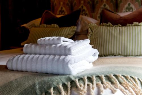 three white towels stacked on a bed with pillows at Clover in Wrenbury