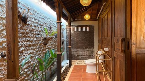 a bathroom with a toilet and a brick wall at Umah Nayoye Amed in Ambat