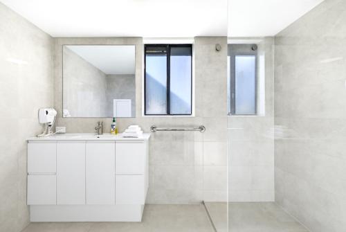 a white bathroom with a sink and a shower at Belaire Place Motel Apartments in Caloundra