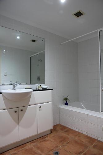 a white bathroom with a sink and a tub at Darwin Deluxe Apartments in Darwin