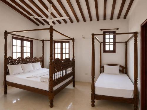 two wooden beds in a room with two windows at Jannataan Hotel in Lamu