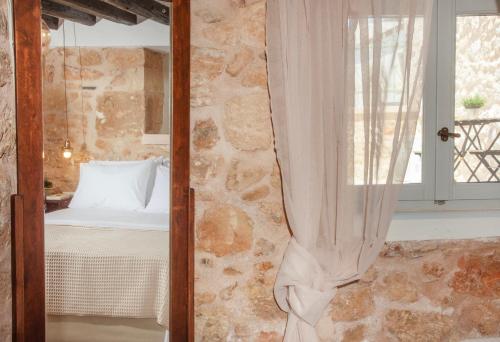 a bedroom with a stone wall with a bed and a window at Amalthea Guest House in Egina