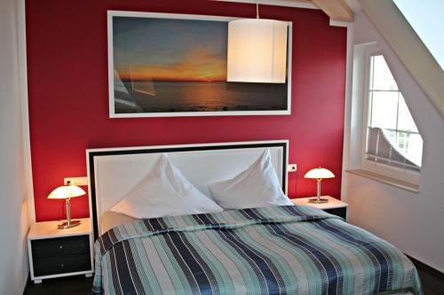 a bedroom with a red wall with a bed and two lamps at Seeperle in Dranske