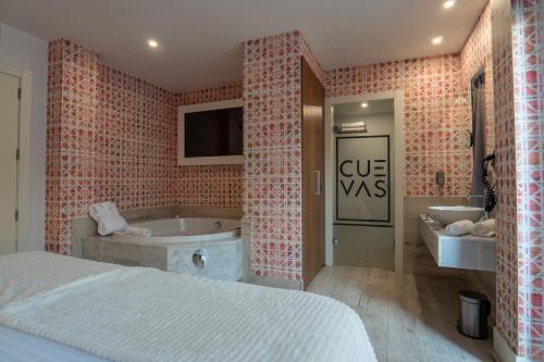a bedroom with a bed and a tub and a sink at Hotel Cuevas - Adults Only in Santillana del Mar